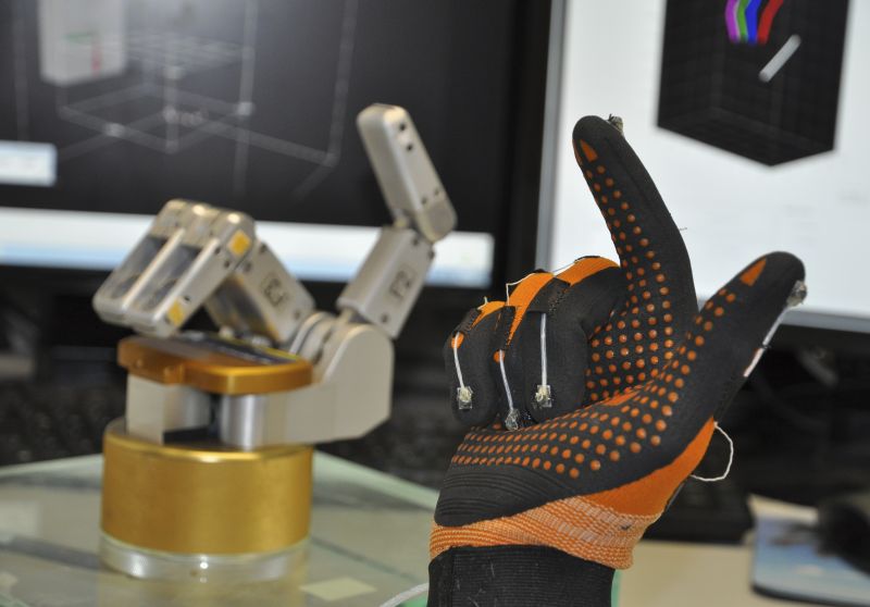 Versuchsaufbau am Deutschen Primatenzentrum: Ein Datenhandschuh mit magnetischen Sensoren an den Fingerkuppen misst die Fingerbewegungen einer Versuchsperson, welche auf eine Roboterhand übertragen werden. Foto: Stefan Schaffelhofer